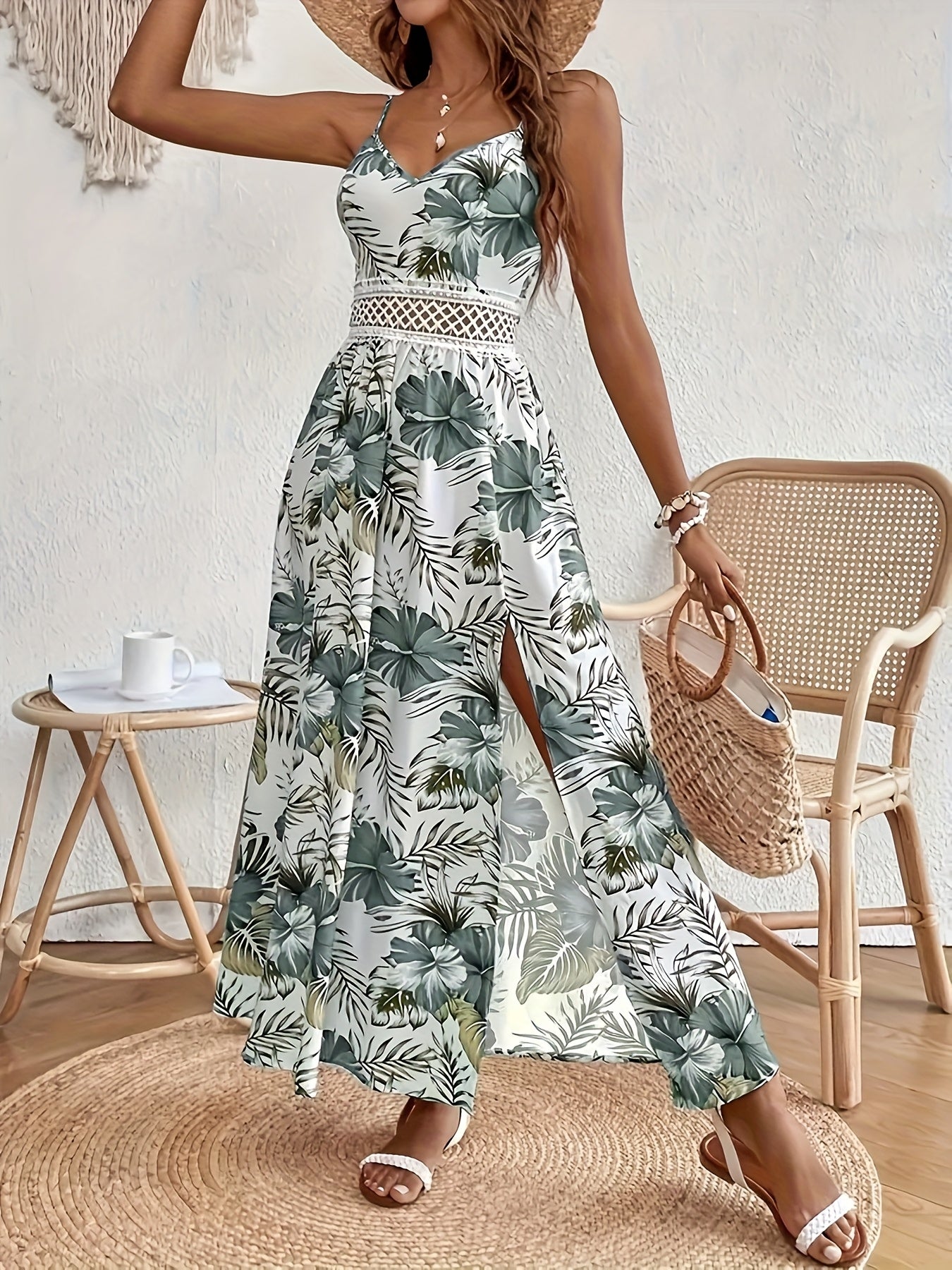 Woman sitting in a white maxi dress with green tropical leaf print, featuring a crochet waist panel and high front slit.