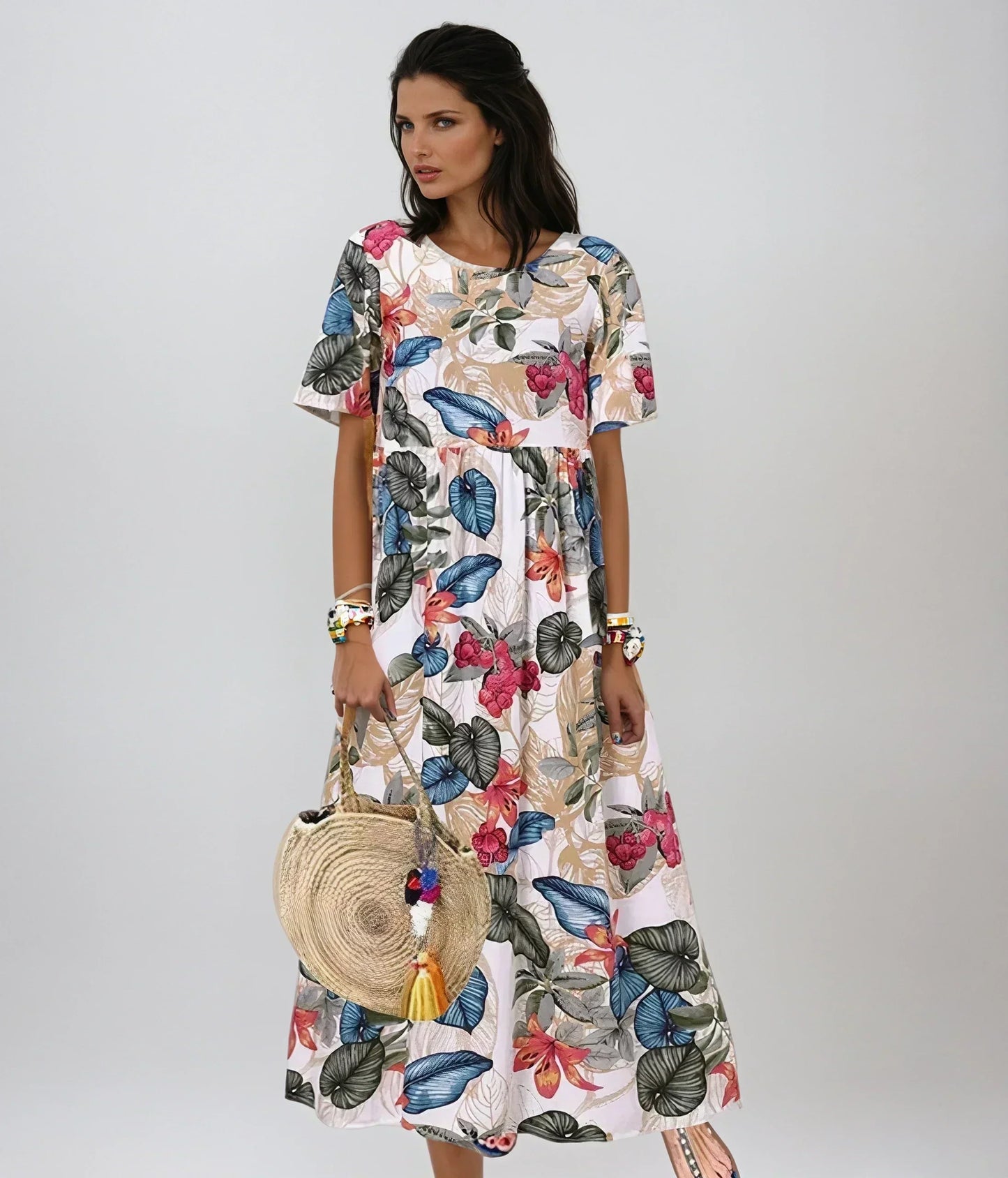 Beige - A woman wearing a navy blue maxi dress with a vibrant pink, orange, and green tropical floral print, featuring short sleeves, a crewneck, and an empire waist, holding a round woven straw bag.
