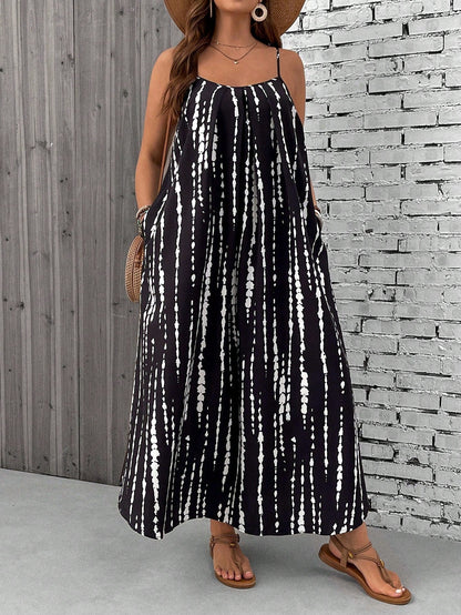 Black-And-White - A woman stands on a sandy beach wearing a sleeveless maxi dress with a bold green, pink, and yellow tropical leaf print, featuring spaghetti straps and side pockets.