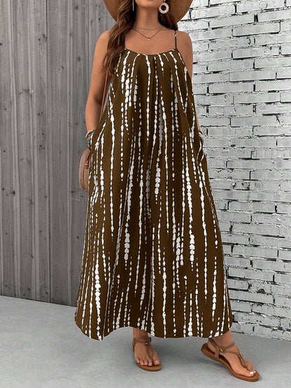 Brown - A woman stands on a sandy beach wearing a sleeveless maxi dress with a bold green, pink, and yellow tropical leaf print, featuring spaghetti straps and side pockets.