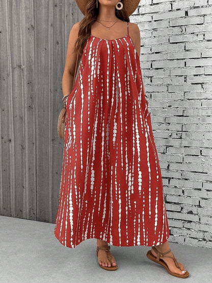 Burgundy - A woman stands on a sandy beach wearing a sleeveless maxi dress with a bold green, pink, and yellow tropical leaf print, featuring spaghetti straps and side pockets.