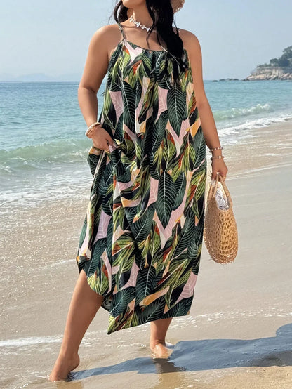 Versatile Colors - A woman stands on a sandy beach wearing a sleeveless maxi dress with a bold green, pink, and yellow tropical leaf print, featuring spaghetti straps and side pockets.