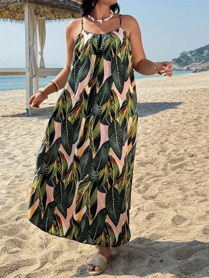 Versatile Colors - A woman stands on a sandy beach wearing a sleeveless maxi dress with a bold green, pink, and yellow tropical leaf print, featuring spaghetti straps and side pockets.