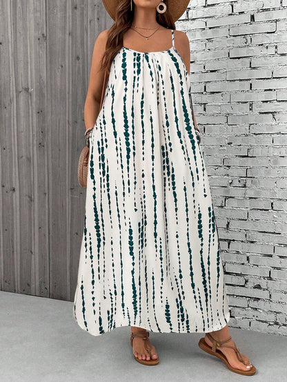 Apricot - A woman stands on a sandy beach wearing a sleeveless maxi dress with a bold green, pink, and yellow tropical leaf print, featuring spaghetti straps and side pockets.