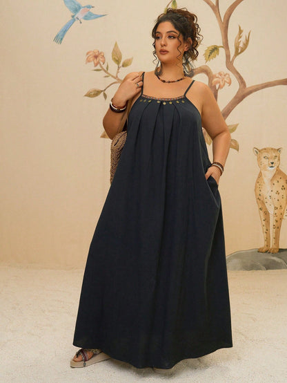 Black - A woman stands on a sandy beach wearing a sleeveless maxi dress with a bold green, pink, and yellow tropical leaf print, featuring spaghetti straps and side pockets.